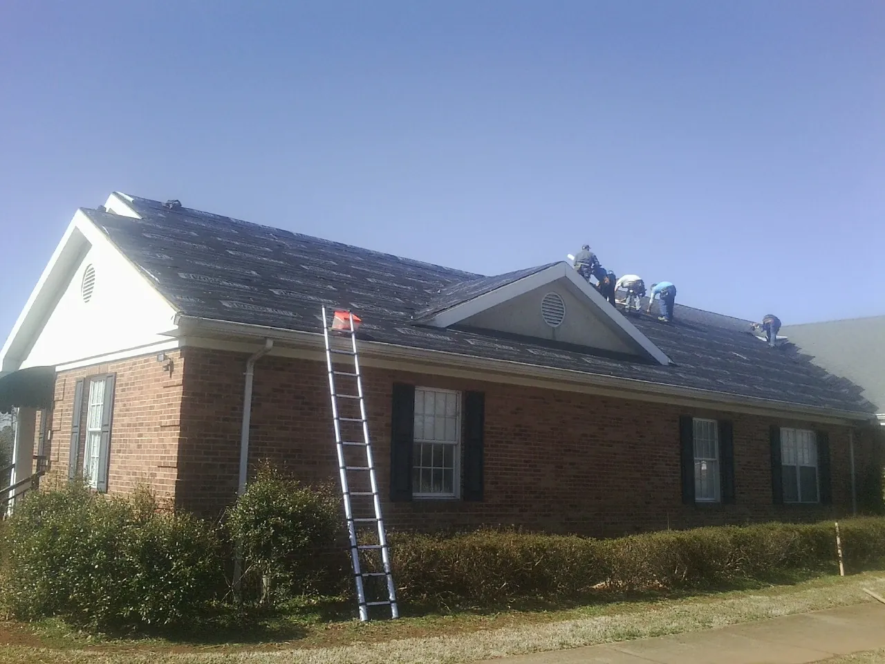 Crew tearing shingles off a brick ranch roof with a ladder set — Metal Roof Repair work by our crew in College Place