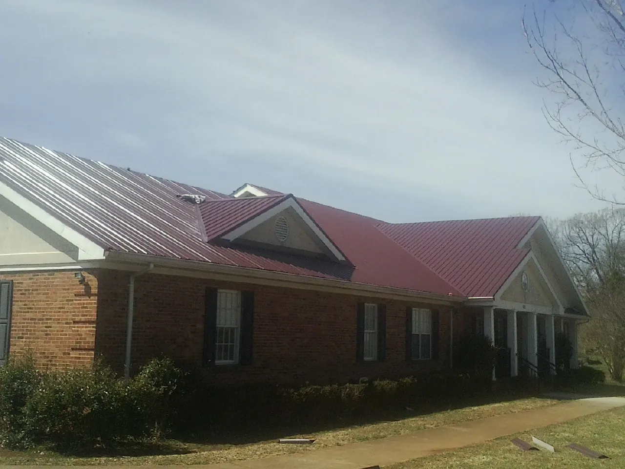 Red metal roof with gabled entries on a long brick building, from a Hail Damage Roof Repair job in College Place