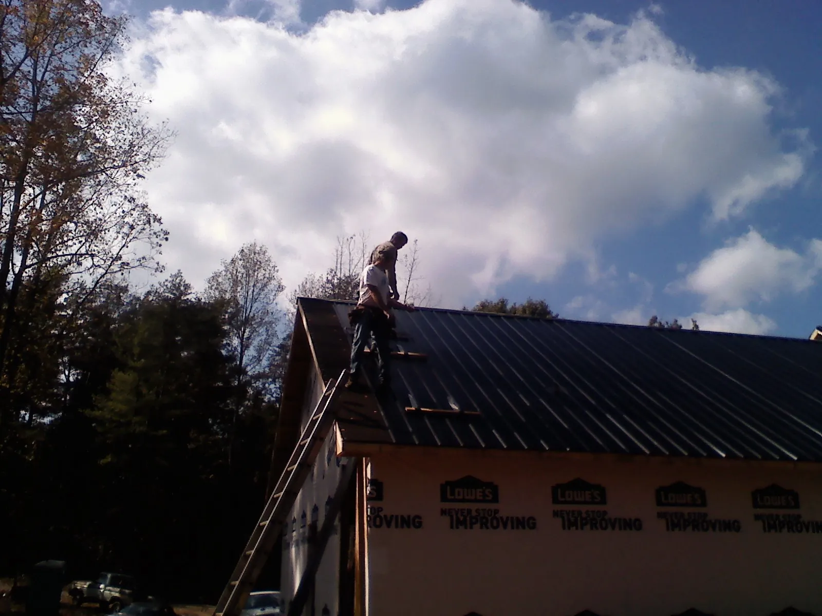 Roofer fastening dark metal panels high against a cloudy sky, from a Roof Inspection job in College Place