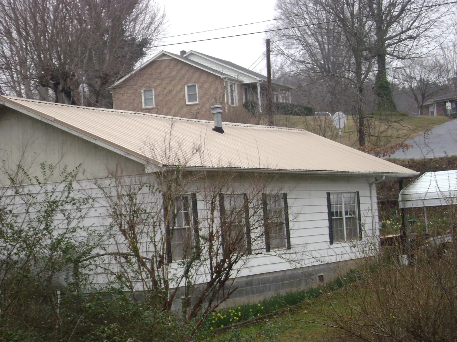 Tan metal roof on a white sided house set into a hillside — Commercial Roofing by Roofing Brothers in College Place